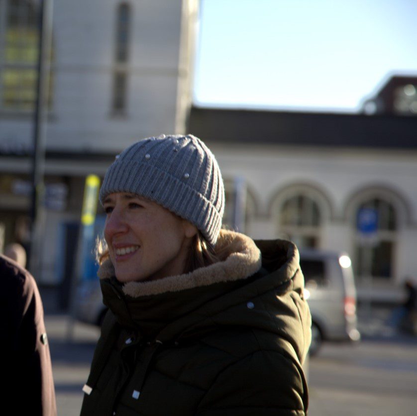 Louise Parlons Bentata, wearing a grey hat and green coat smiles at the camera