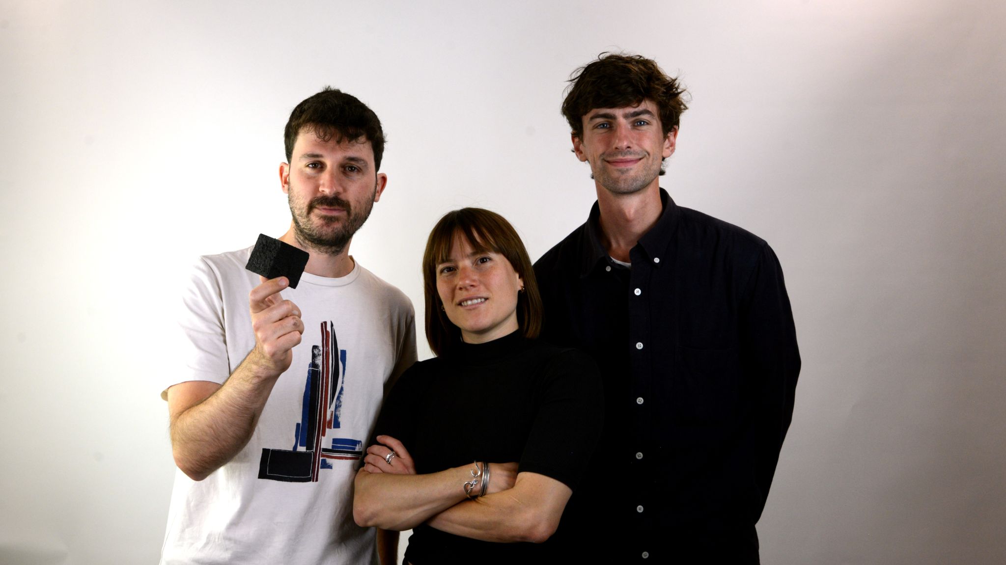 Three teammembers look at the camera holding a block of biochar
